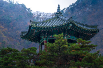 Fototapeta premium Traditional Korean pavilion Wollyujeong perched on a rocky cliff of Wollyubong peak surrounded by colorful autumn forest in morning mist, Yeongdong, South Korea.