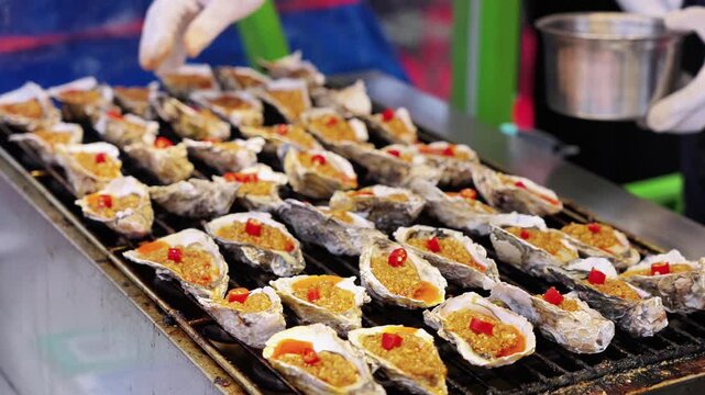 Fresh oysters topped with garlic and chili being grilled on a metal barbecue, prepared for serving.