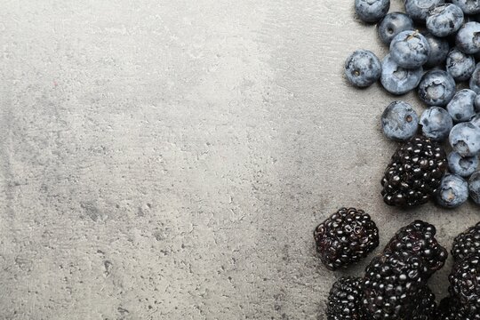 Fresh ripe blackberries and blueberries on grey table, flat lay. Space for text