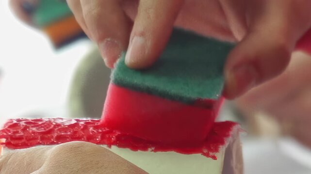 Close-up of hands delicately applying a rich, vibrant red textured design onto a pristine white dessert roll. This careful embellishment transforms the sweet treat into a delightful culinary artistry.