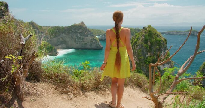 Woman with long braid walking on cliff edge overlooking Diamond Beach in Nusa Penida Indonesia
