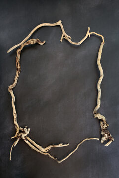 Driftwood wreath rustic minimal zen frame decoration on mottled gray brown background. Decorative art border design of organic seaside twisted curved wood.
