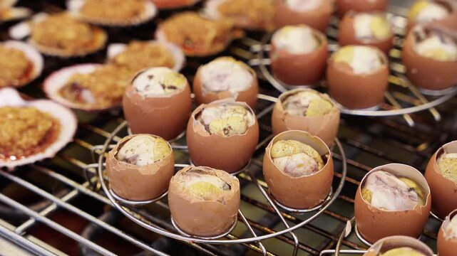 Baked eggs in eggshells and stuffed scallops with toppings, arranged on a metal cooking rack for serving.