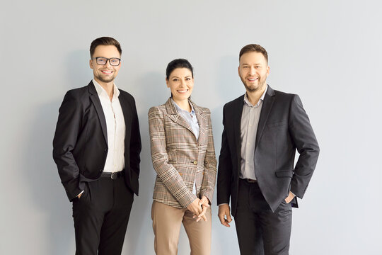 Team businesspeople portrait of confident managers. Three executives and professionals smile against light gray copy space, ideal for company site and recruitment. Clear theme of leadership unity.