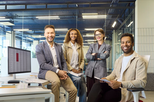 Office team colleagues portrait, business people smiling. Modern glass workplace with computer and desk documents shows teamwork as the group prepares for a meeting. Clear concept of team unity.