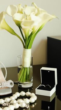 Vertical video. Bridal accessories with white calla lilies, wedding rings and pearls on a table.