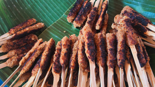 Traditional Indonesian Balinese sate lilit grilled minced meat satay skewers served on a banana leaf