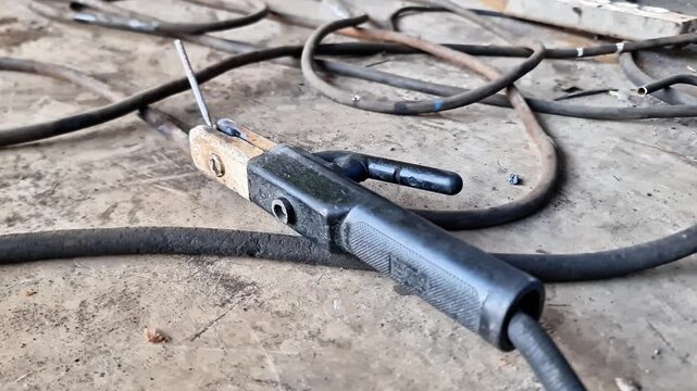 Close up of heavy duty welding electrode holder gripping a welding rod on a workshop floor.