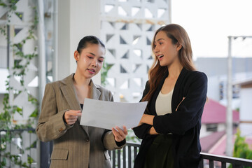 Obraz premium Asian businesswomen discussing project documents on an office balcony