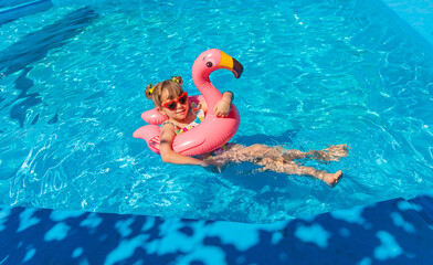 Naklejka premium A child swims in a pool surrounded by flamingos. Selective focus.
