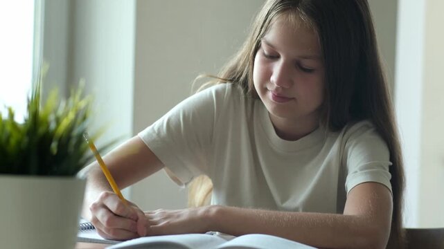 Smiling young girl writing in notebook with yellow pencil during home studies. Concept of education and homework