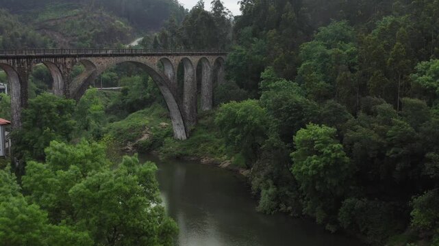 Aerial view of Poco de Santiago Bridge spanning the river surrounded by lush green forest in Sever do Vouga, Aveiro District, Portugal.