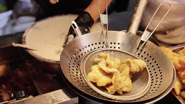 Cooking scene showing fried battered food in metal strainers, with preparation of batter on a griddle nearby.