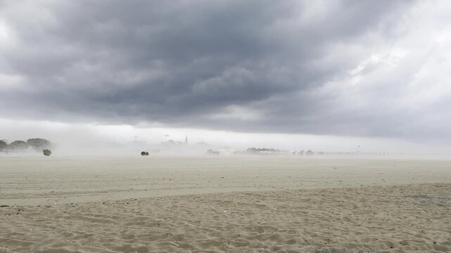 A sudden sandstorm hits a beach. Powerful wind gusts lifting sand across the shore as severe summer weather and storm clouds approach after a heatwave. Grado, Italy - July 1, 2026.