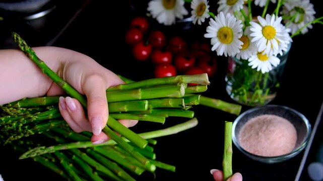 Female hand trimming fresh asparagus by snapping off tough ends before cooking preparing tender green spears for healthy homemade meals and simple recipes