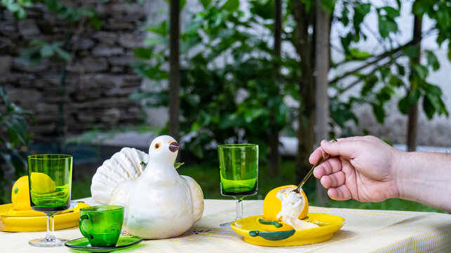 Hand taking a spoonful of a gourmet lemon-shaped dessert on a garden table