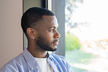 Pensive young man looking out window in natural light, thoughtful portrait of quiet reflection © Daniel