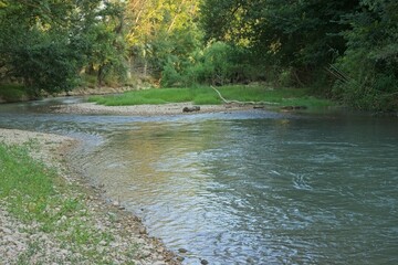 Natural river winding through a green forest with a gravel shore  Description: A scenic view of a calm river flowing and bending through a lush woodland. Features a rocky pebble shoreline in the foreg © silvia