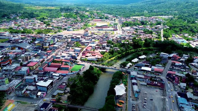 Wide Drone View of Tropical Ecuador Town with River, Bridge, Green Hills, Roads and Urban Buildings, South American Travel Landscape