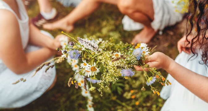 Young women weaving a wildflower wreath before a traditional summer solstice ceremony. Hands creating a floral crown from fresh meadow flowers, celebrating midsummer customs.