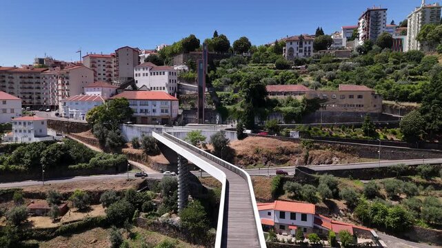 Aerial view of the modern Carpinteira Pedestrian Bridge spanning the valley with urban buildings and lush greenery in Covilha, Castelo Branco District, Portugal.