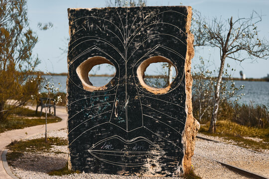 Deltebre, Spain - May 25, 2026: An outdoor stone decorative tribal mask totem monument standing on a path in the Ebro Delta natural park in Catalonia.