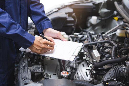 Auto check, car service shop concept. Automobile repairman writing job checklist on clipboard, mechanic checking engine to estimate repair machine, inspecting maintenance by engineer at vehicle garage