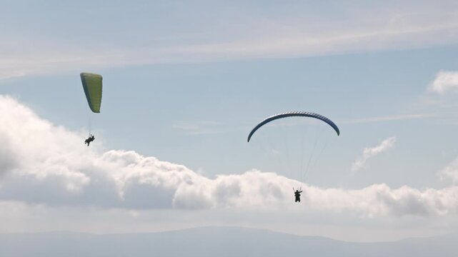 People try paragliding flying with parachutes against clouds