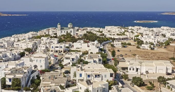 Naousa Paros Greece Aerial v2 low flyover small village capturing faneromeni church surrounded by beautiful coastal whitewashed buildings with paros park hilltop in the background - September 2021