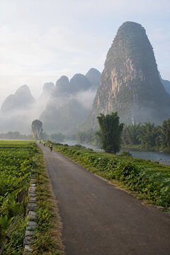 Quiet rural road leading toward misty karst mountains and green fields.generative AI