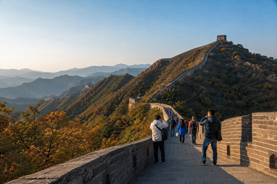 Tourists walking along the Great Wall on a sunlit mountain ridge in autumn.generative AI