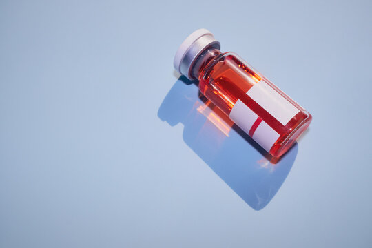 Vial containing red liquid for vaccine or treatment, casting blue shadow