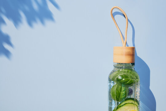 Glass water bottle showing refreshing detox infused water with basil and cucumber on blue background