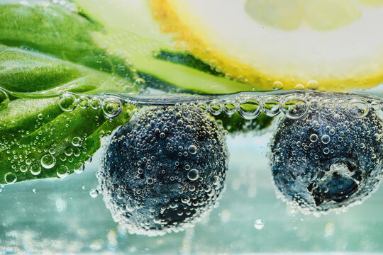 Blueberries, lemon slice and basil leaves infusing in clear carbonated water with bubbles