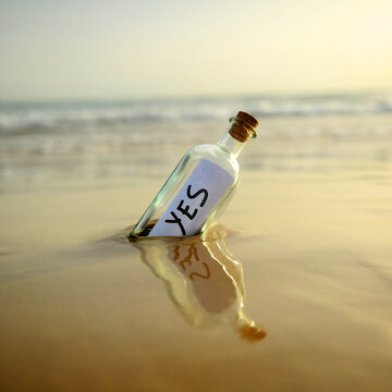 Yes message in a bottle at sunset. Bottle on the beach, washed ashore by the tide, affirmative answer sent. Affirmative response. Background of a misty beach with gentle waves in a square format.