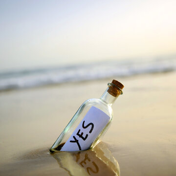 Yes, at dawn. Message in a bottle on beach, washed ashore by the tide, containing affirmative answer. Positive message sent. Misty beach landscape at sunrise with soft waves out of focus and blurred