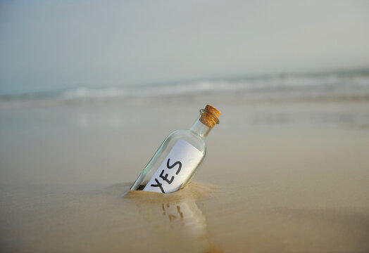 Bottle on the beach with an affirmative answer inside, yes, positive message. Affirmative response sent. Misty beach landscape background with gentle waves