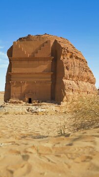 Tomb Lihyan Son of Kuza at Hegra, Saudia Arabia, low ground view vertical video, dry shrubs moving in calm wind near, sandy desert landscape around