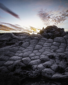 Aerial view of White Pocket featuring unique brain rock formations and a person standing on sandstone under a dramatic sunset sky in Coconino County, Arizona, United States.