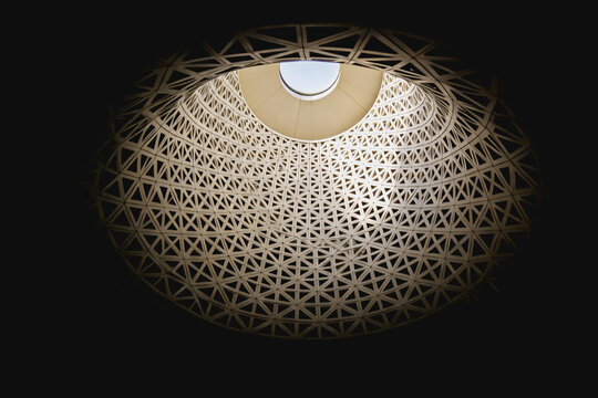 A low-angle view of an intricate geometric lattice dome ceiling with a central skylight, showcasing architectural structural design.