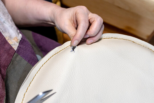 craftswoman sews up hole in leather seat of chair