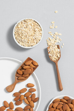 Rolled oats and almonds in wooden scoops and bowls on a light gray