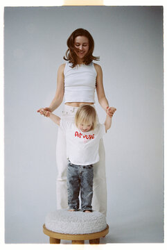 Mother stands behind child holding hands in studio setting