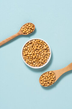 Wooden spoons and bowl filled with dried soybeans on a light blue