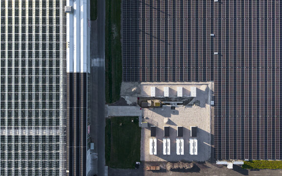 Aerial view of a large solar farm with rows of photovoltaic panels adjacent to a modern greenhouse complex in Middenmeer, North Holland, Netherlands.