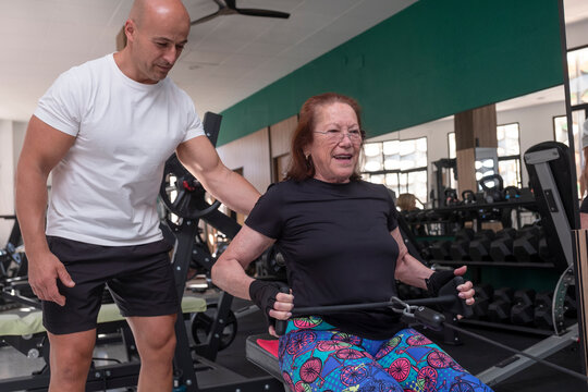Senior woman and personal trainer on rowing machine correcting posture