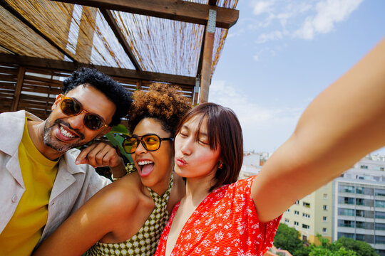 Cheerful friends enjoying rooftop selfie on sunny day