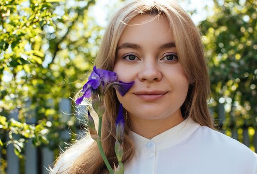 Portrait of blond smiling woman with violet flower outdoors