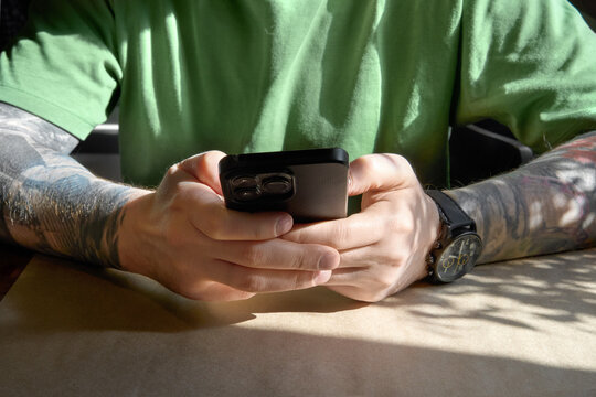 Close up of a tattoed person using smartphone in a sunlit interior.