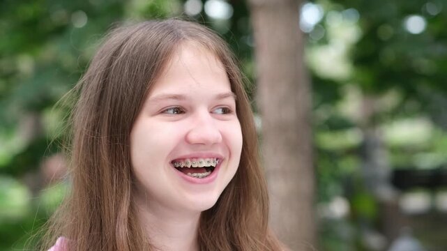 Happy laughing caucasian teen girl with dental braces. Positive teenager outdoors in park